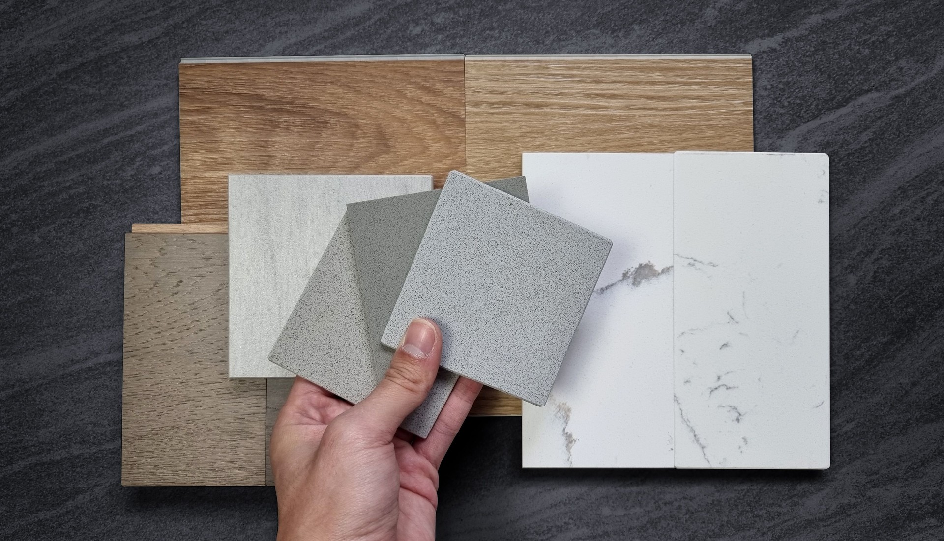 interior designer picking material samples. mood and tone board including wooden vinyl flooring tiles, white marble quartzs, engineering flooring tiles, stone tile, grainy artificial stones.